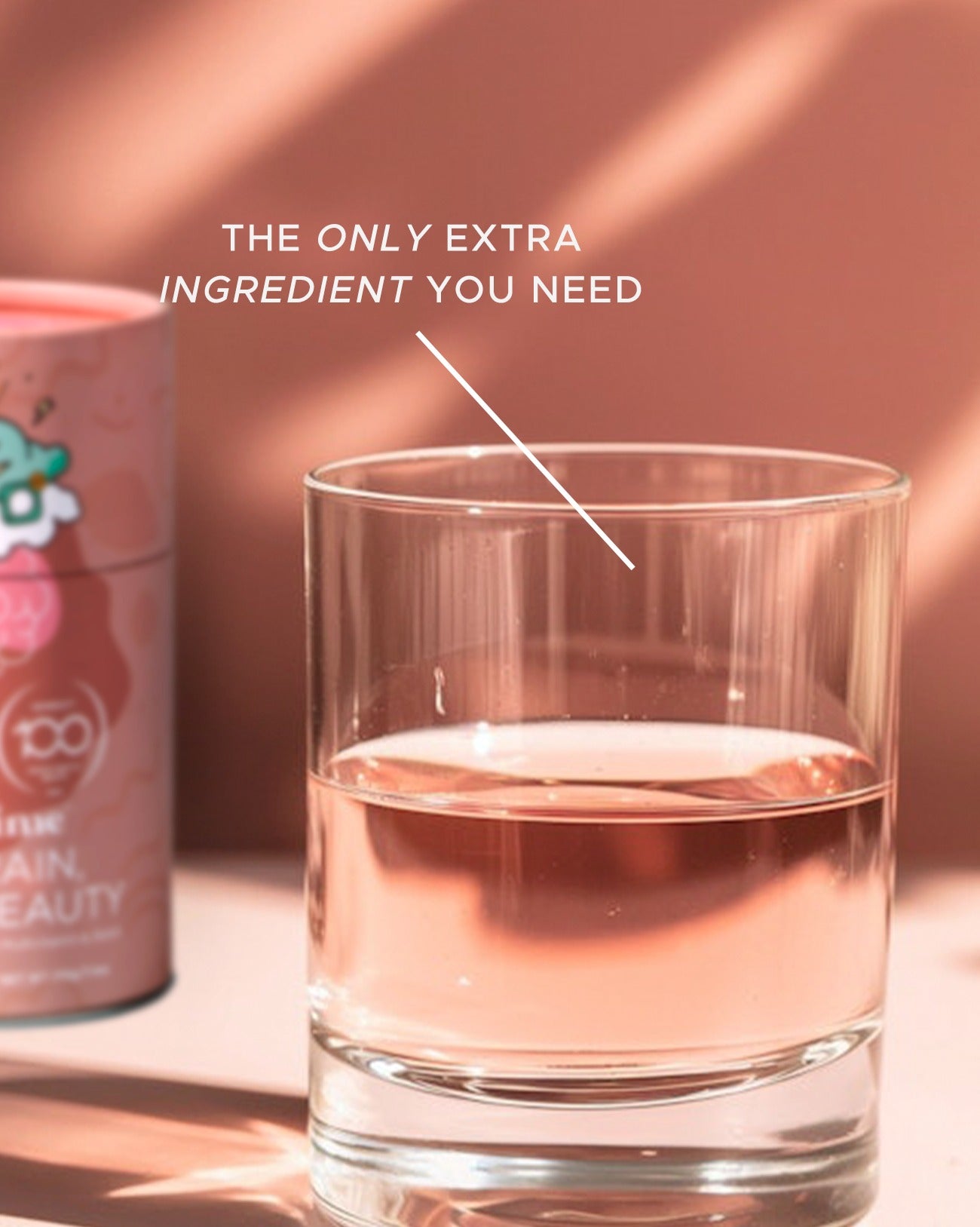 Glass of pink liquid with a can labeled 'The Only Extra Ingredient You Need' on a pink background