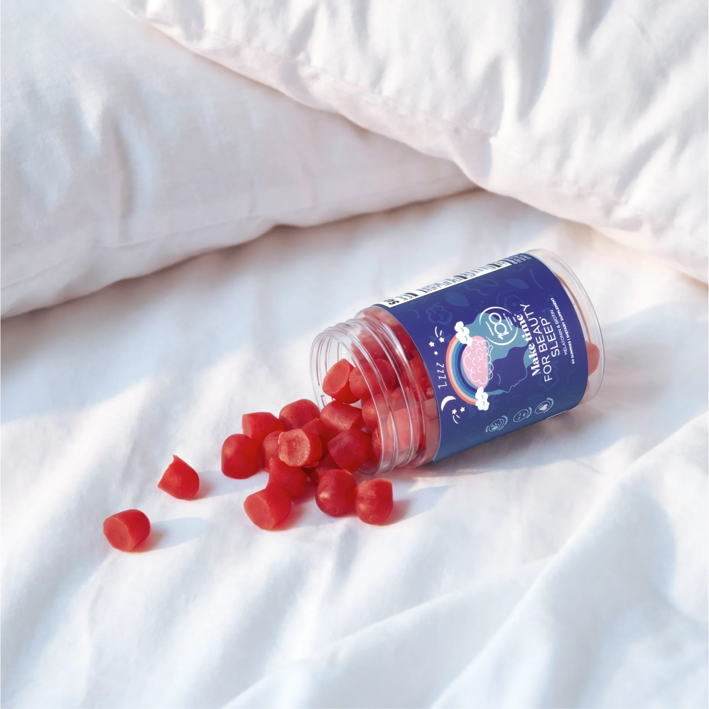 Make Time Beauty Sleep Gummy jar spilling red gummies on white bedsheets