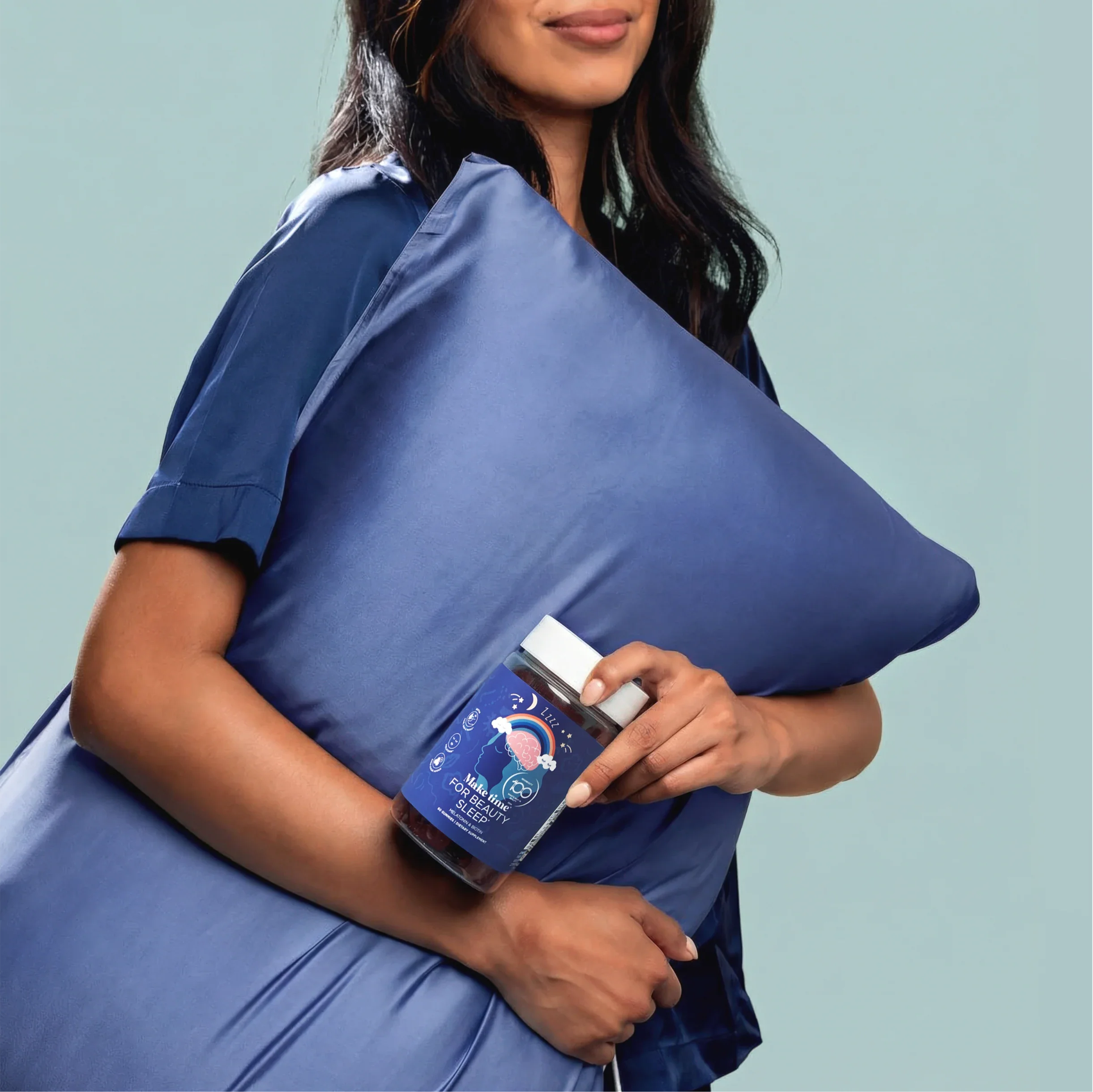 Woman in pajamas holding a pillow and a Make Time Beauty Sleep Gummy jar