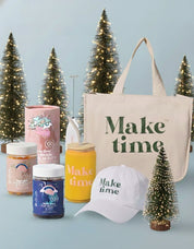 Collection of 'Make time' branded products including a tote bag, hats, and jars with Christmas trees in the background.